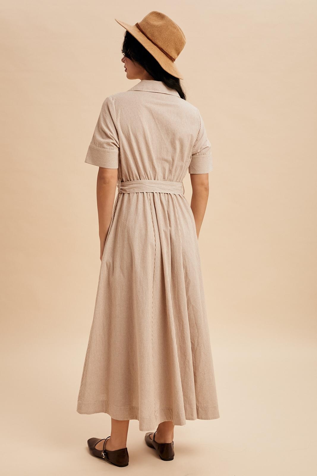 woman wearing a beige striped midi dress with a belted waist and short sleeves, standing with her back to the camera