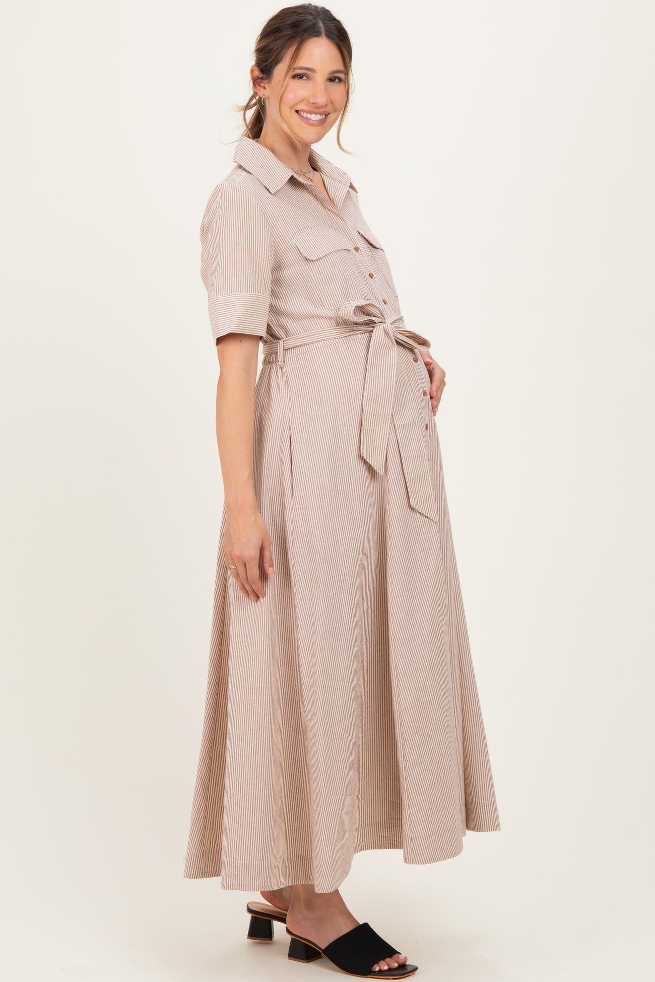 woman wearing a beige striped maternity dress with short sleeves and a tie waist, showcasing her baby bump