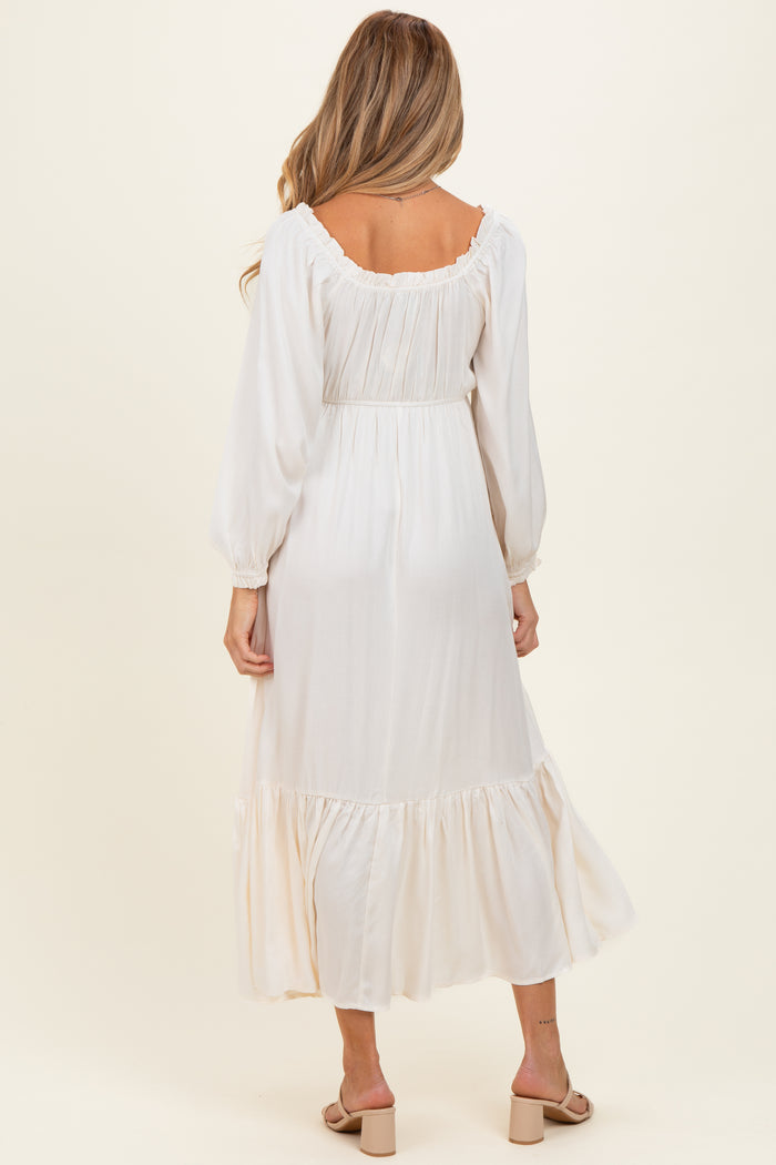 woman wearing a cream long sleeve maternity maxi dress with ruffle details and a cinched waist