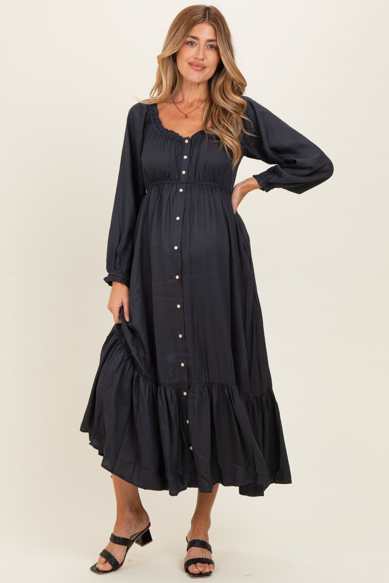 woman wearing a black maternity midi dress with button details and a tiered hem, showcasing her baby bump