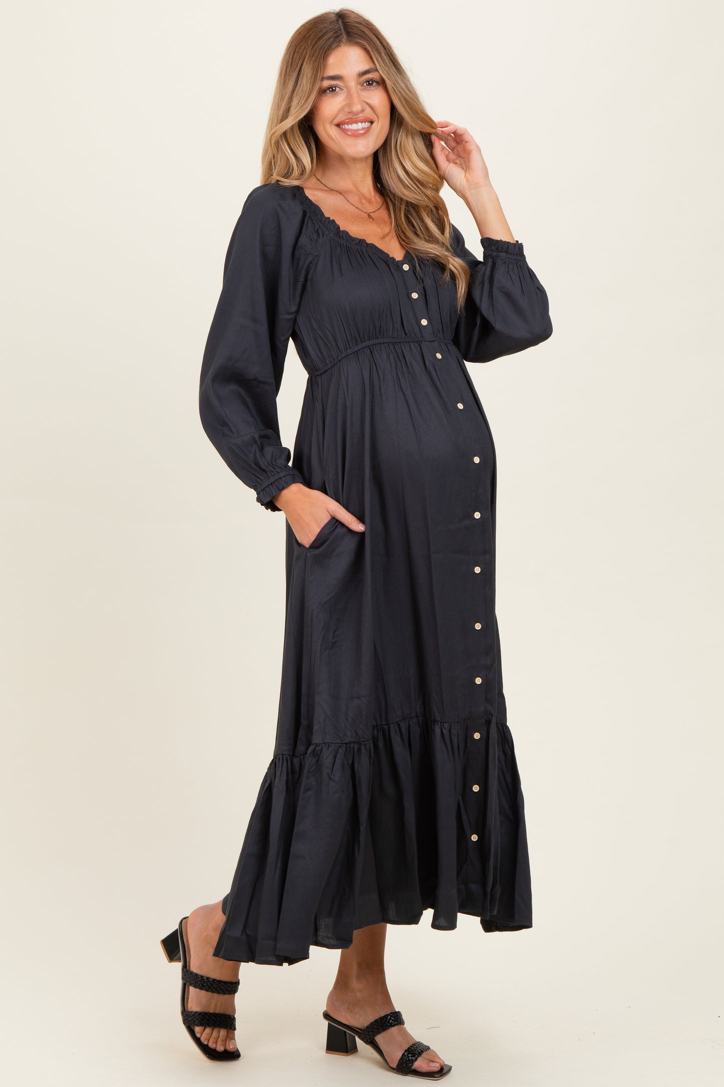 woman wearing a navy blue maternity dress with long sleeves, button front, and ruffled hem, showing baby bump