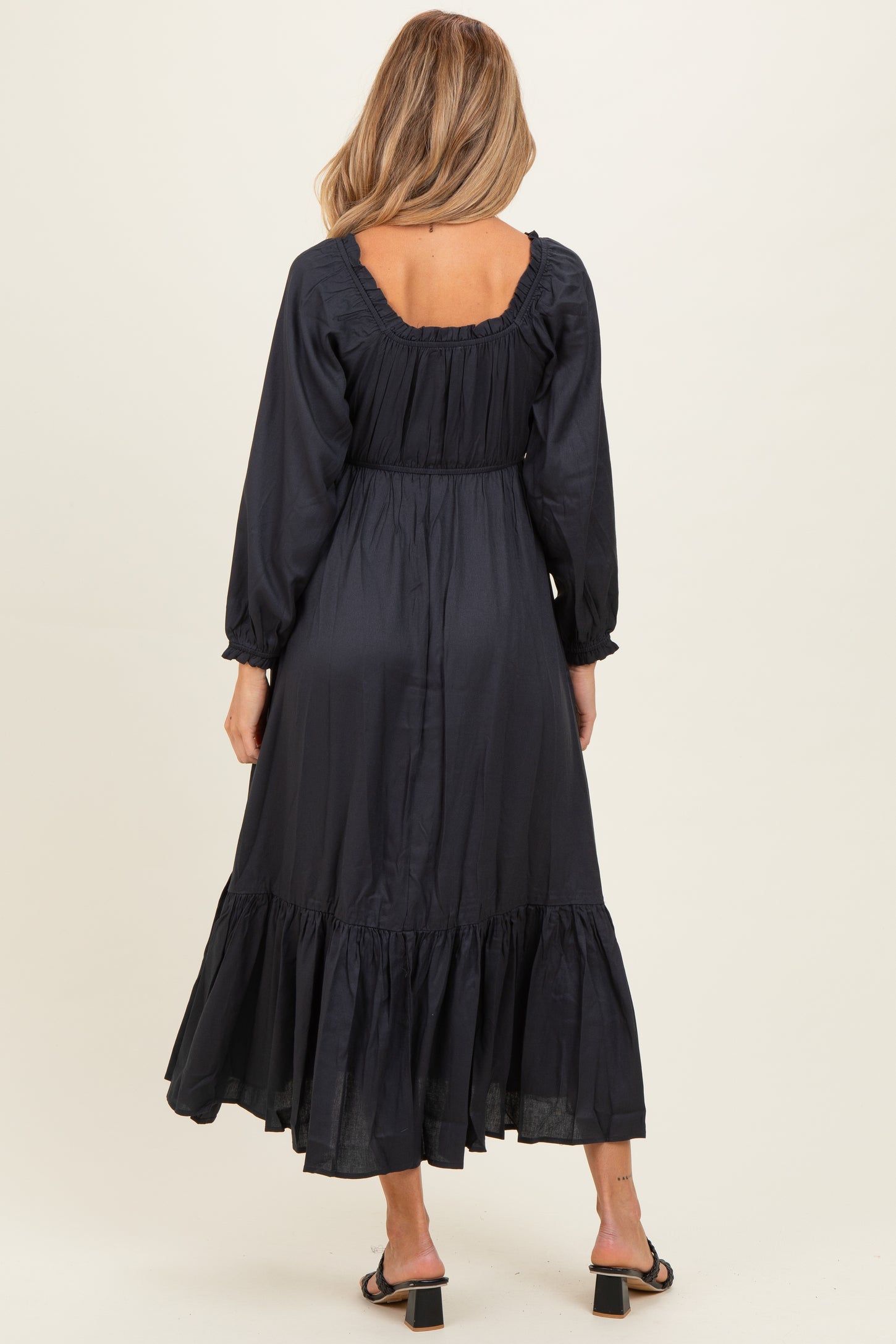 woman wearing a dark navy long sleeve maternity dress with a ruffled hem and open back detail