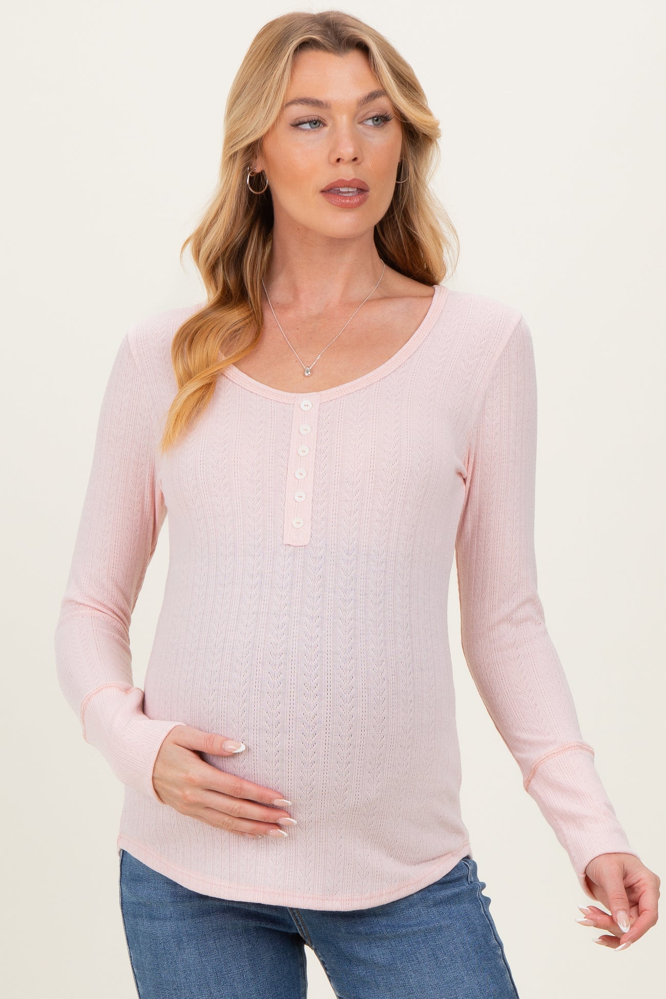 woman wearing a light pink maternity long sleeve top with button details and a visible baby bump