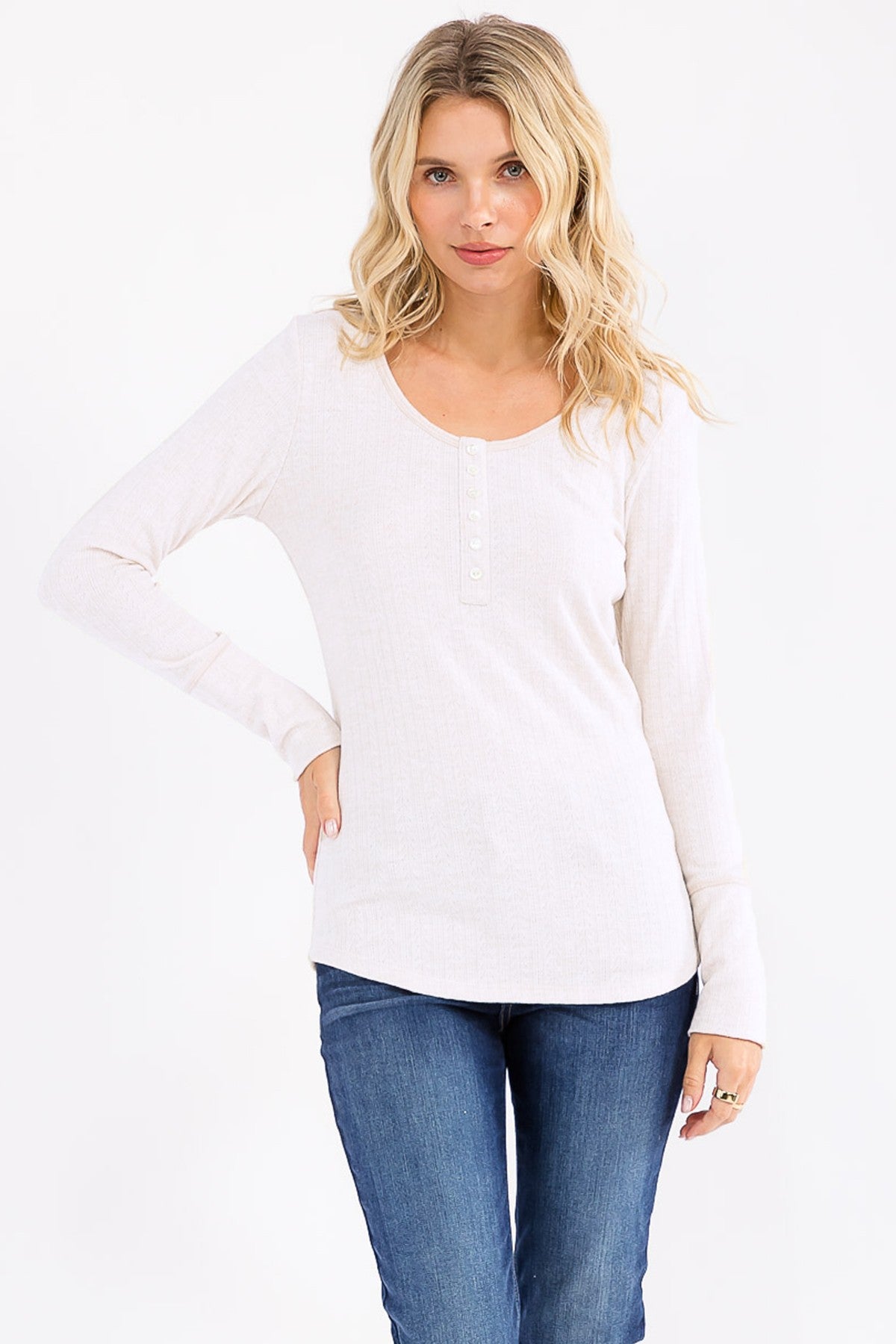 woman wearing a light beige long sleeve henley top with button details and paired with blue jeans