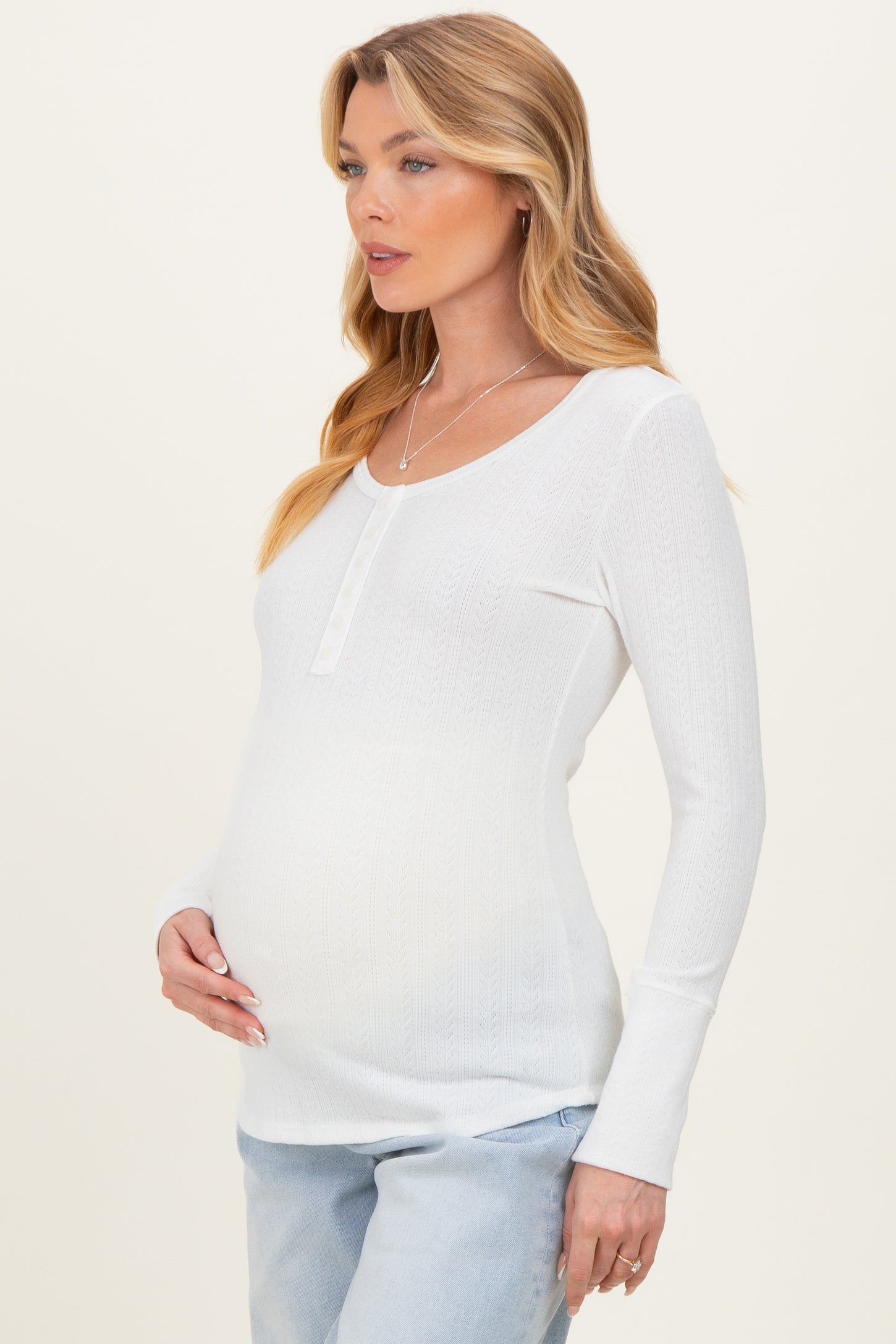 woman wearing a white long sleeve maternity top with a scoop neckline and a visible baby bump