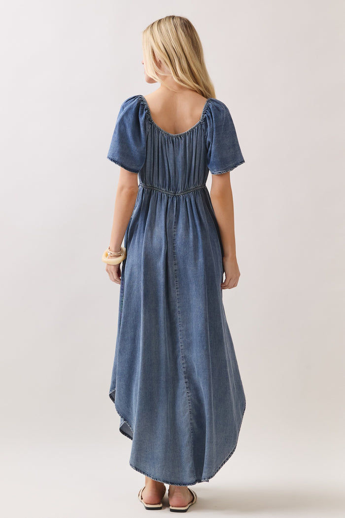 woman wearing a denim maxi dress with short puff sleeves and an elastic waist, viewed from the back