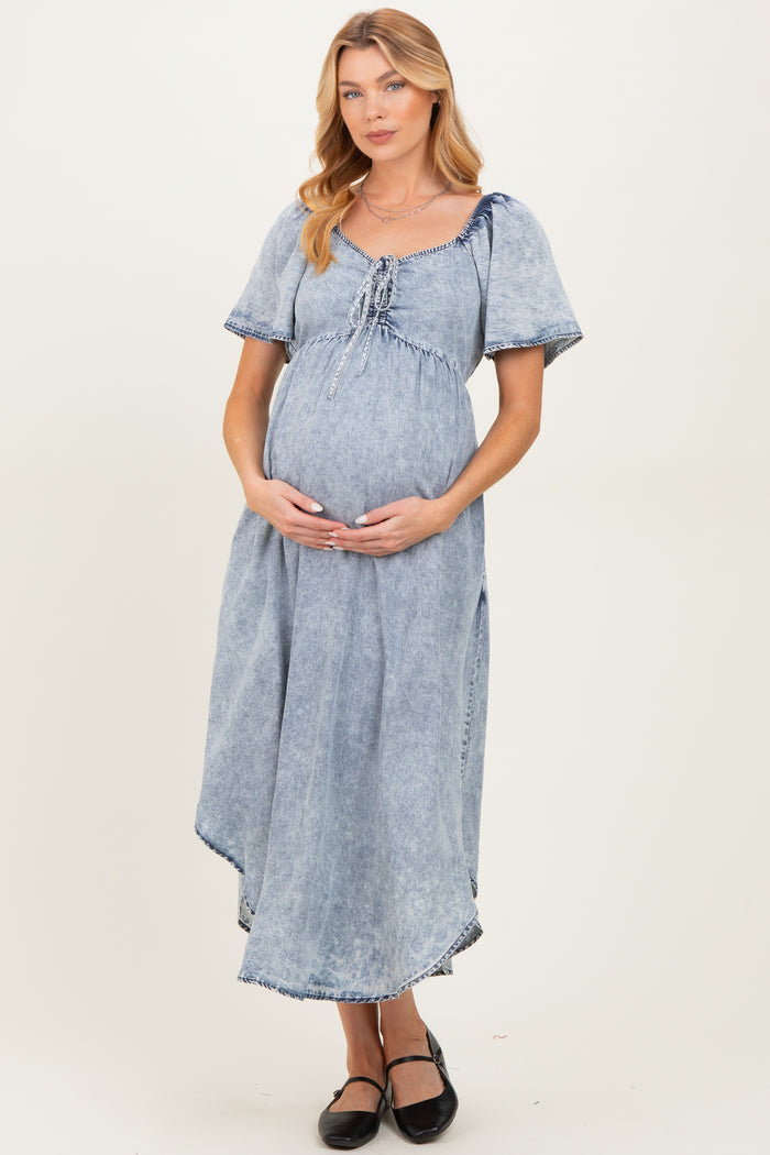 woman wearing a light blue denim maternity dress with a tie detail and holding her baby bump