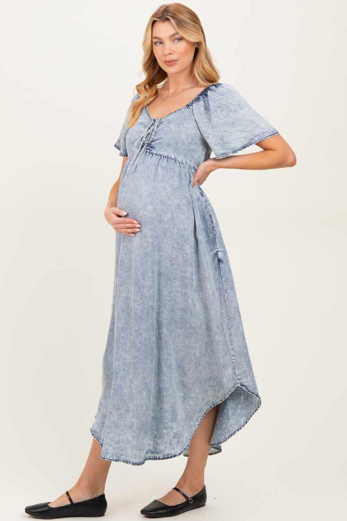 woman wearing a light blue denim maternity dress with short sleeves and a gathered waist, showcasing her baby bump