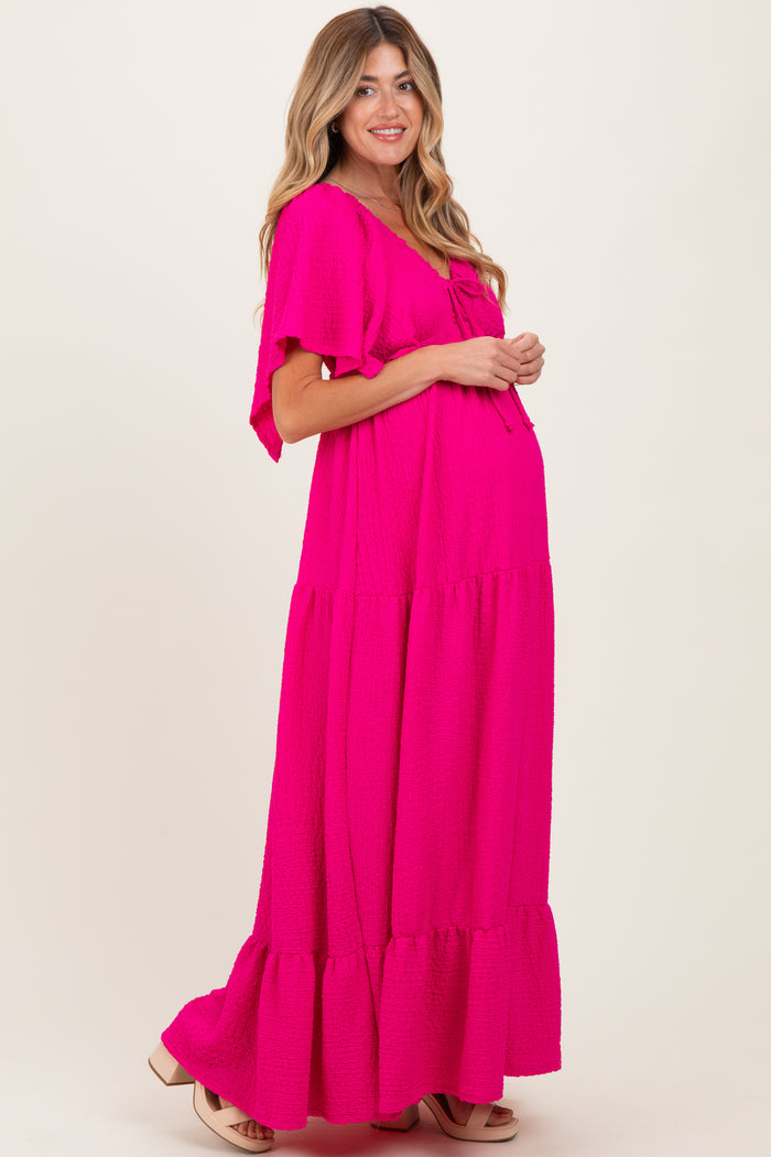woman wearing a bright pink maternity maxi dress with flutter sleeves and a flowing tiered skirt, showing her baby bump