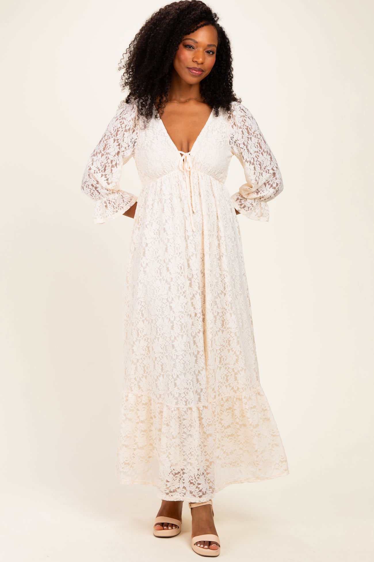 woman wearing a cream lace maxi dress with a deep V-neck and long sleeves, standing against a neutral background
