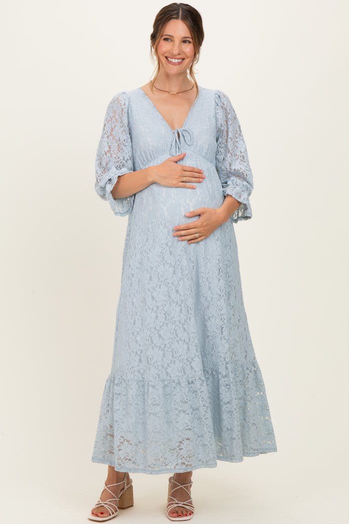 woman wearing a light blue lace maternity dress with a tie front and puff sleeves, cradling her baby bump