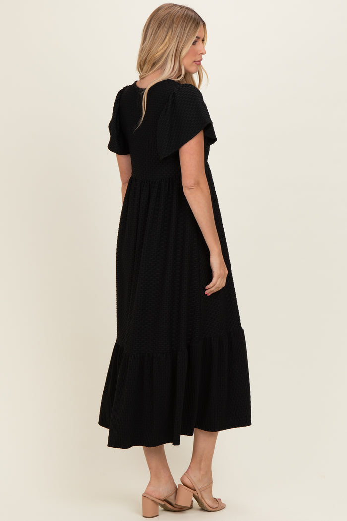 woman wearing a black short sleeve maxi dress with ruffle details, showing the back view and styled with sandals