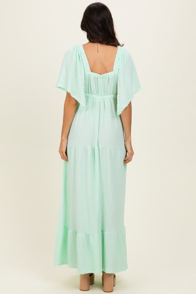 woman wearing a light mint green maxi dress with flutter sleeves and a tiered design, viewed from the back