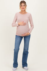 woman wearing a light pink long sleeve ribbed maternity top and blue flared jeans, gently holding her baby bump