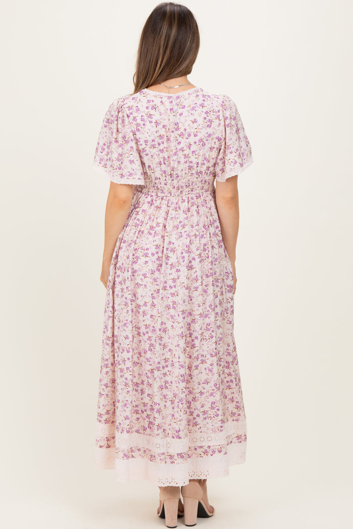 woman wearing a floral print pink maternity dress with short sleeves and a fitted waist, showing a baby bump from the back