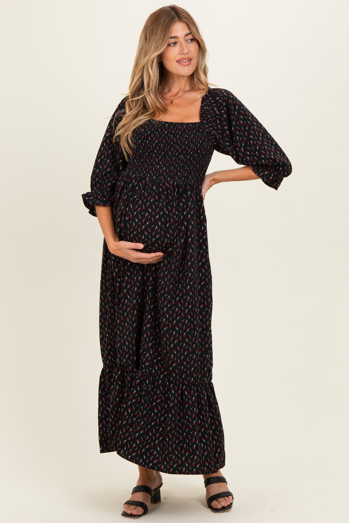 woman wearing a black floral print maternity maxi dress with puff sleeves and holding her baby bump