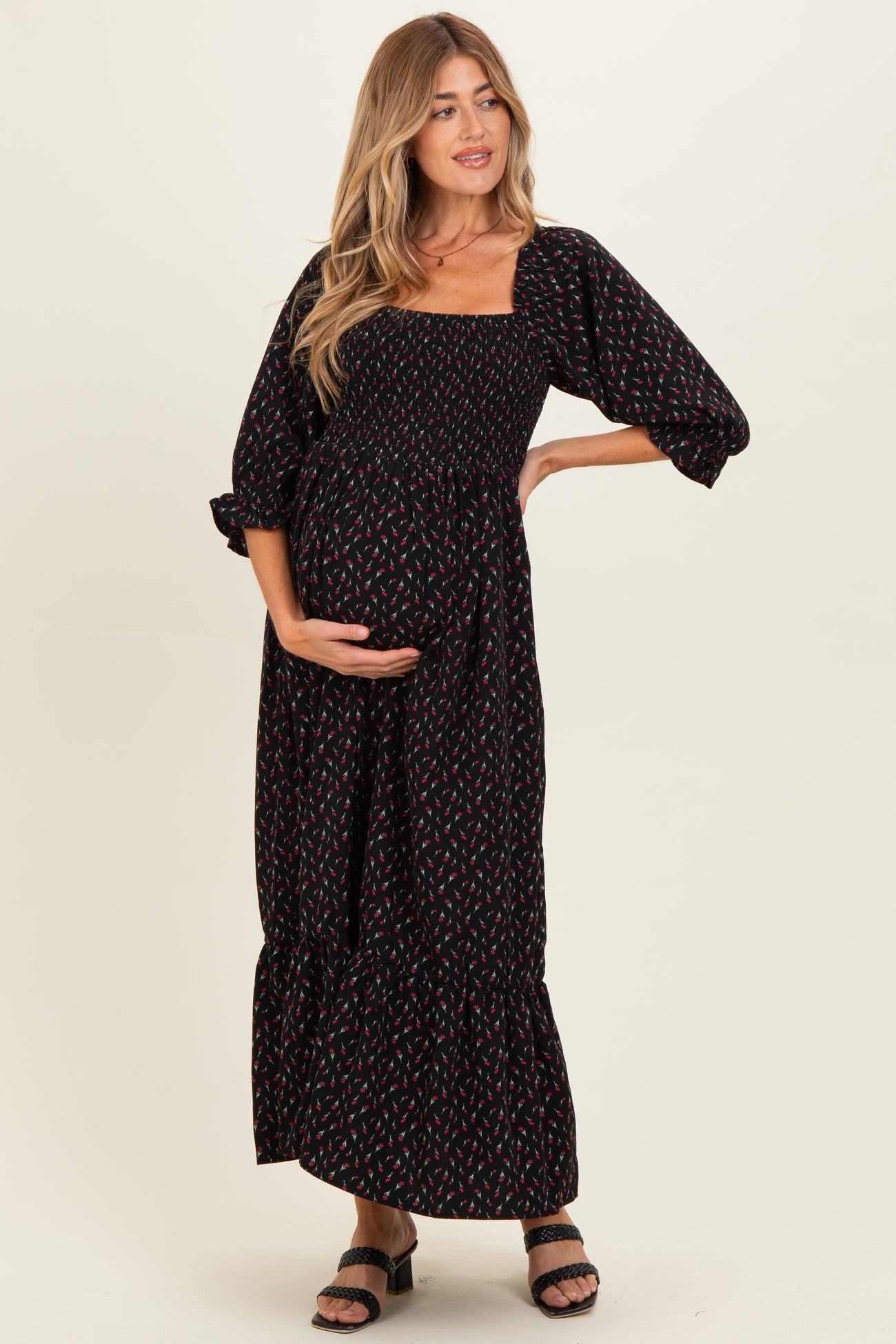 woman wearing a black floral print maternity maxi dress with puff sleeves and holding her baby bump