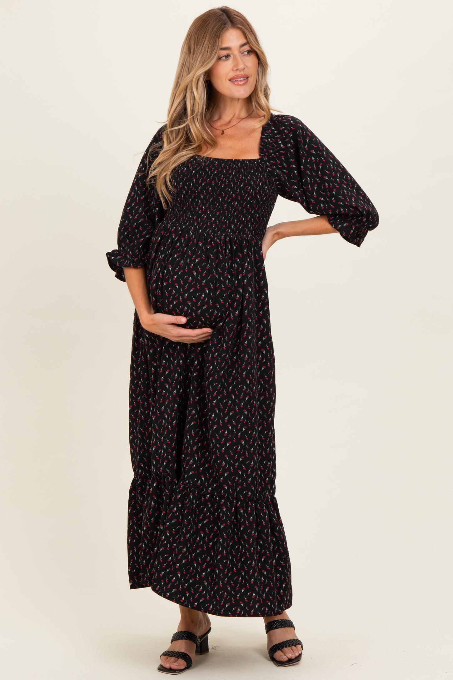 woman wearing a black floral print maternity maxi dress with puff sleeves and holding her baby bump