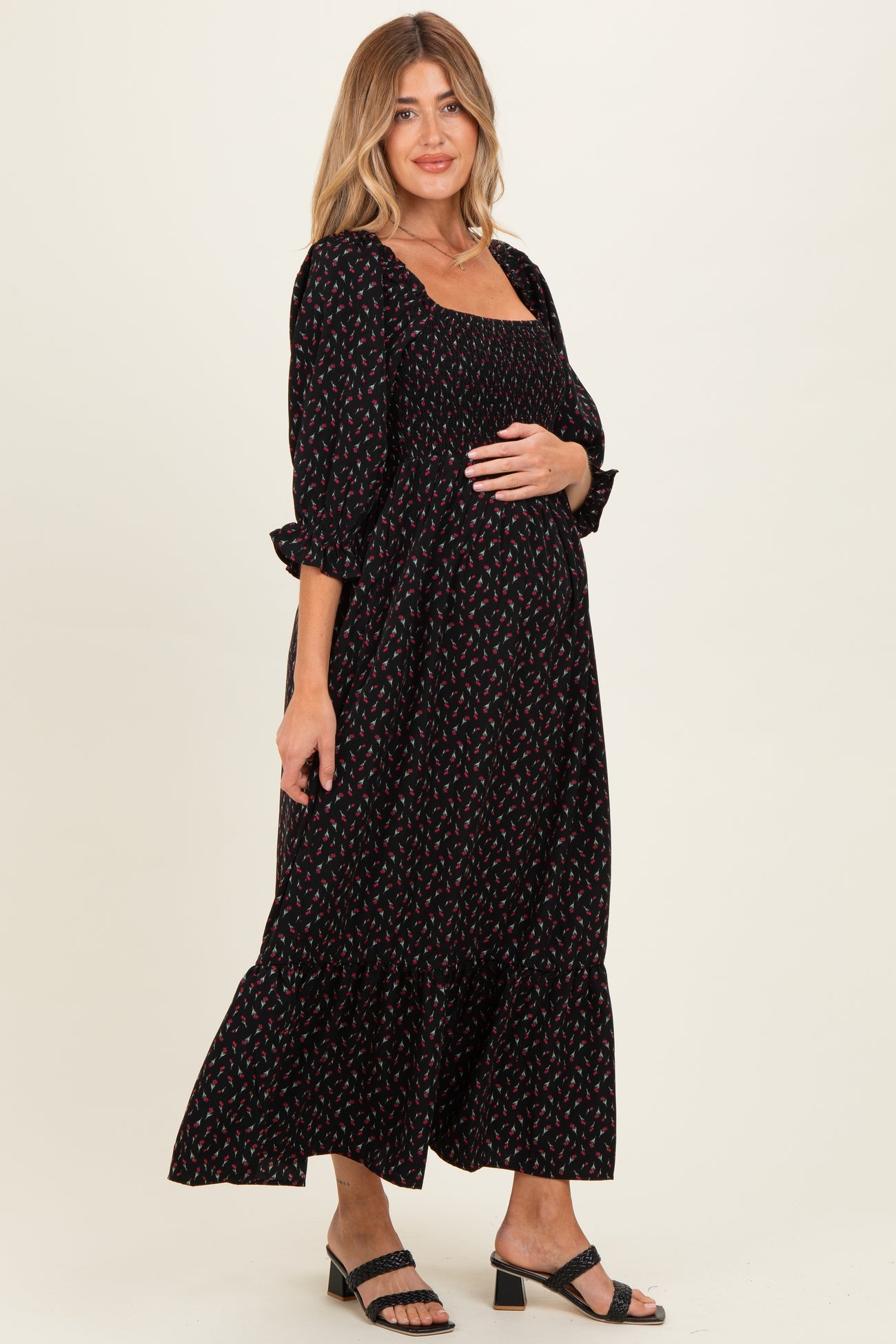 woman wearing a black floral print maternity maxi dress with a square neckline and ruffled sleeves, showing her baby bump