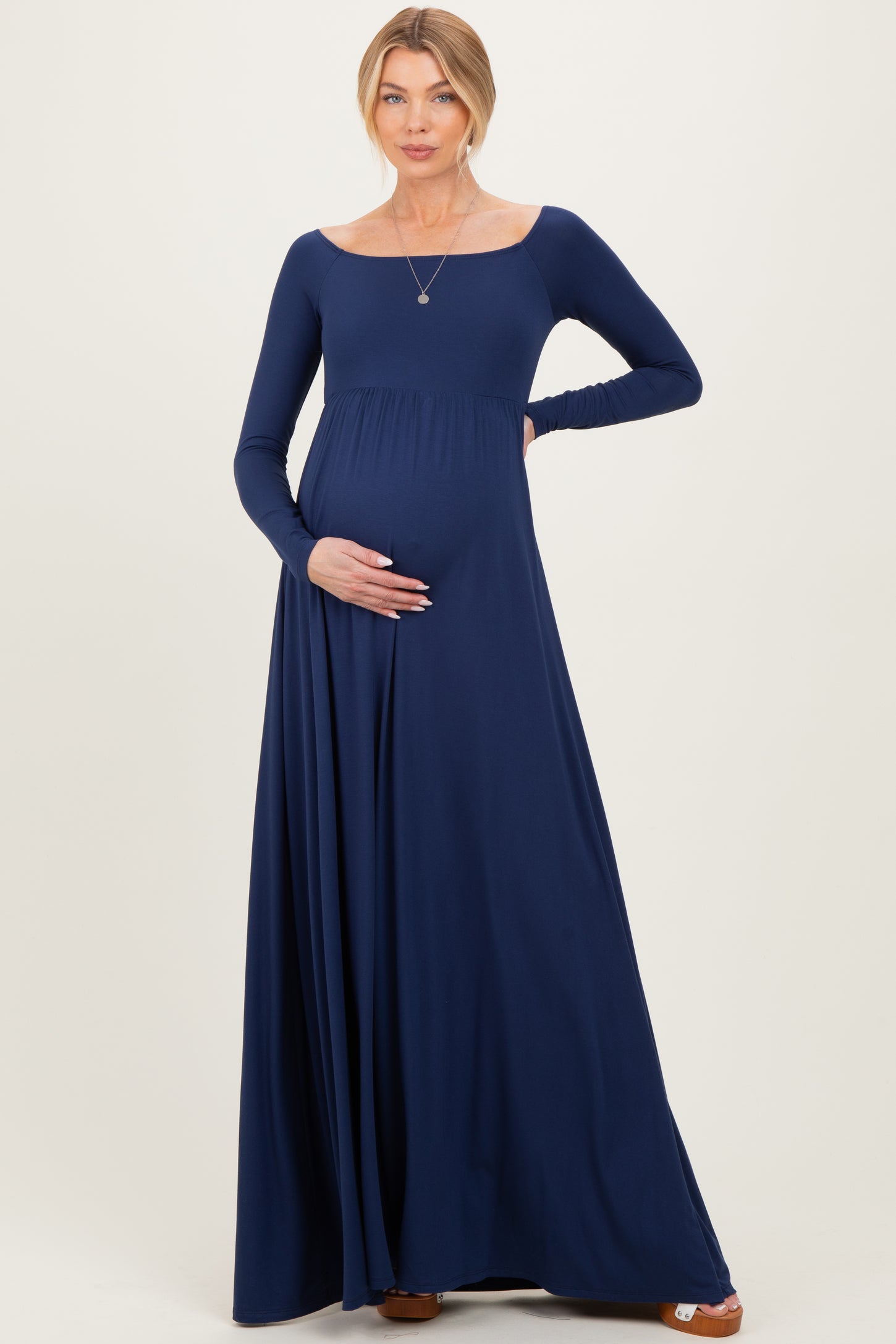 woman wearing a navy blue long sleeve maternity dress with a fitted bodice and flowing skirt, showing her baby bump