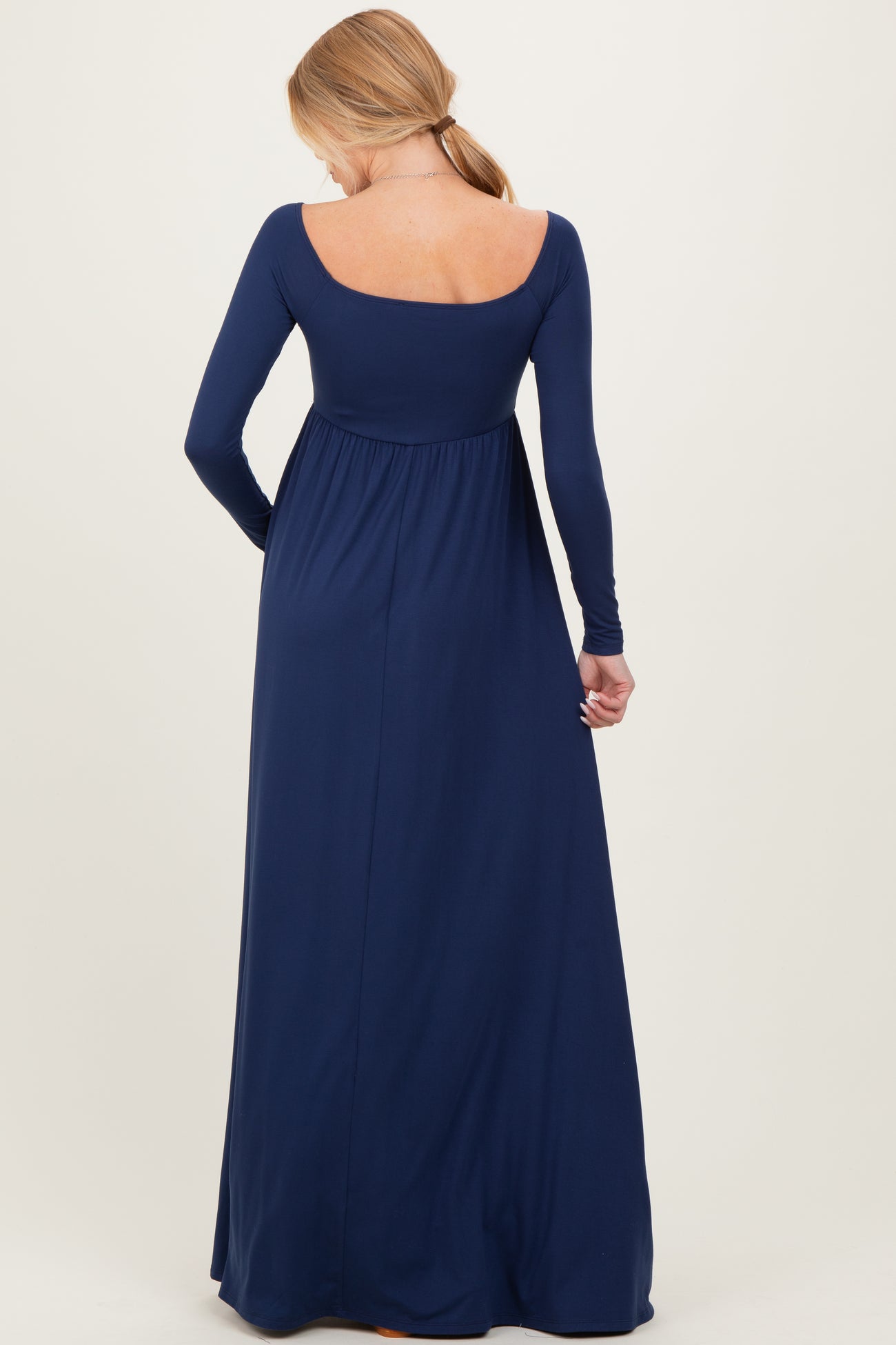 woman wearing a long sleeve navy blue maternity dress, showing the back view and a flowing skirt