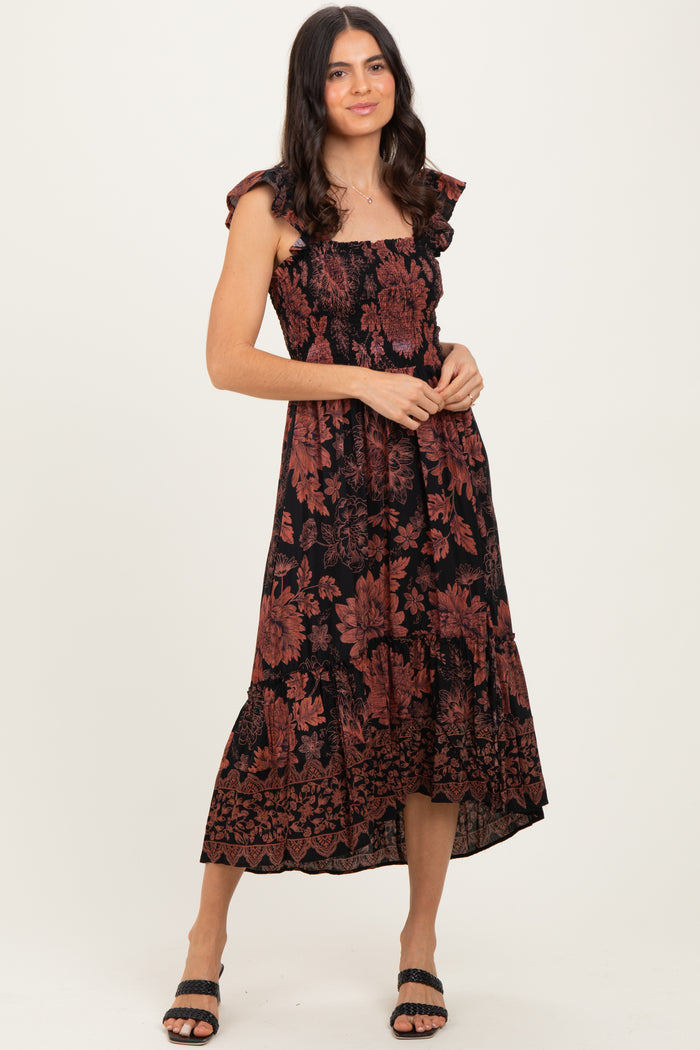 woman wearing a black floral print midi dress with ruffle sleeves and a tiered skirt, standing with a smile