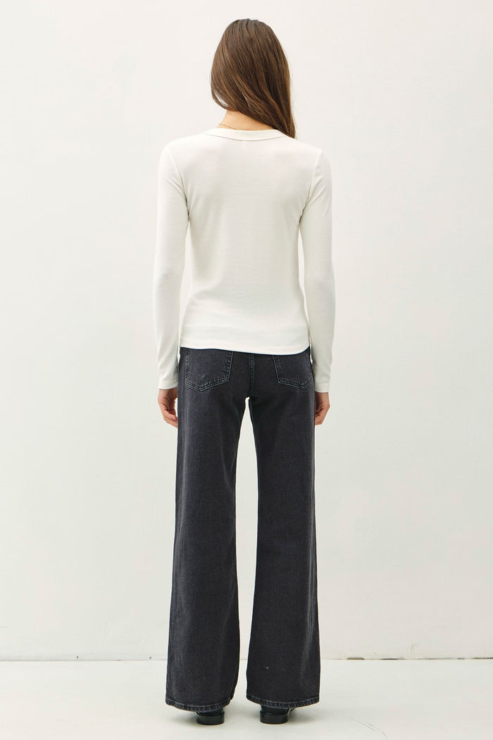 woman wearing a white long sleeve top and black wide-leg jeans, viewed from the back