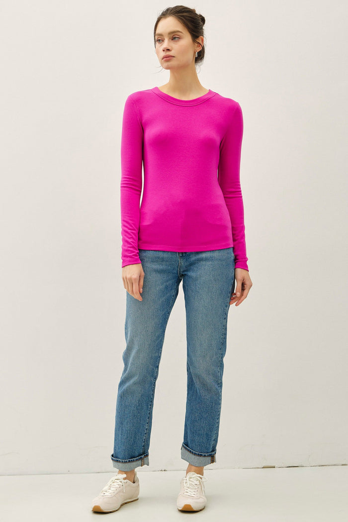 woman wearing a bright pink long sleeve top with a fitted silhouette and light blue rolled cuff jeans