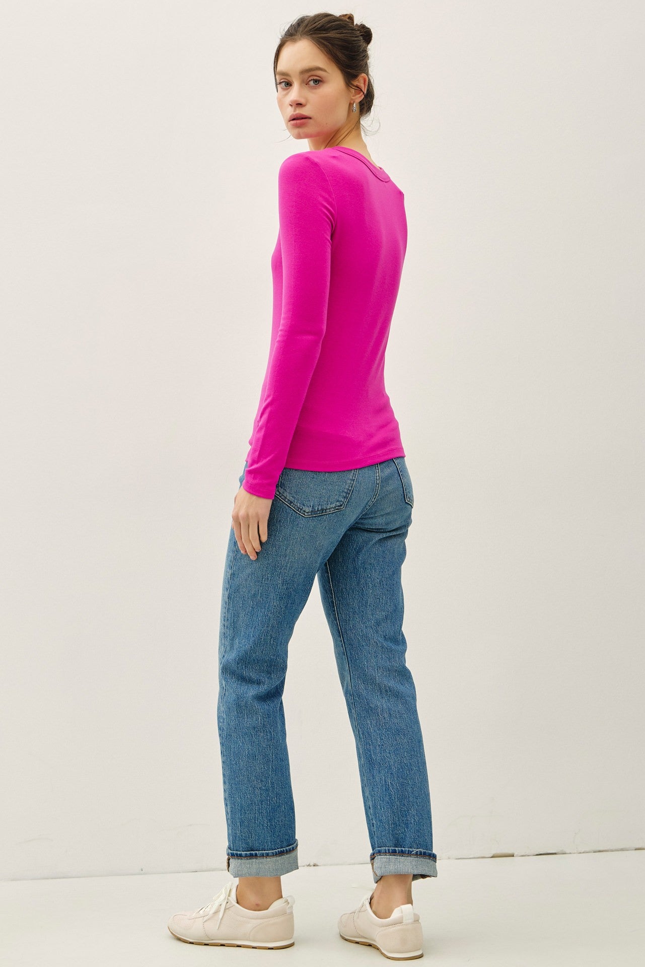 woman wearing a bright pink long sleeve top and light blue jeans, facing away from the camera