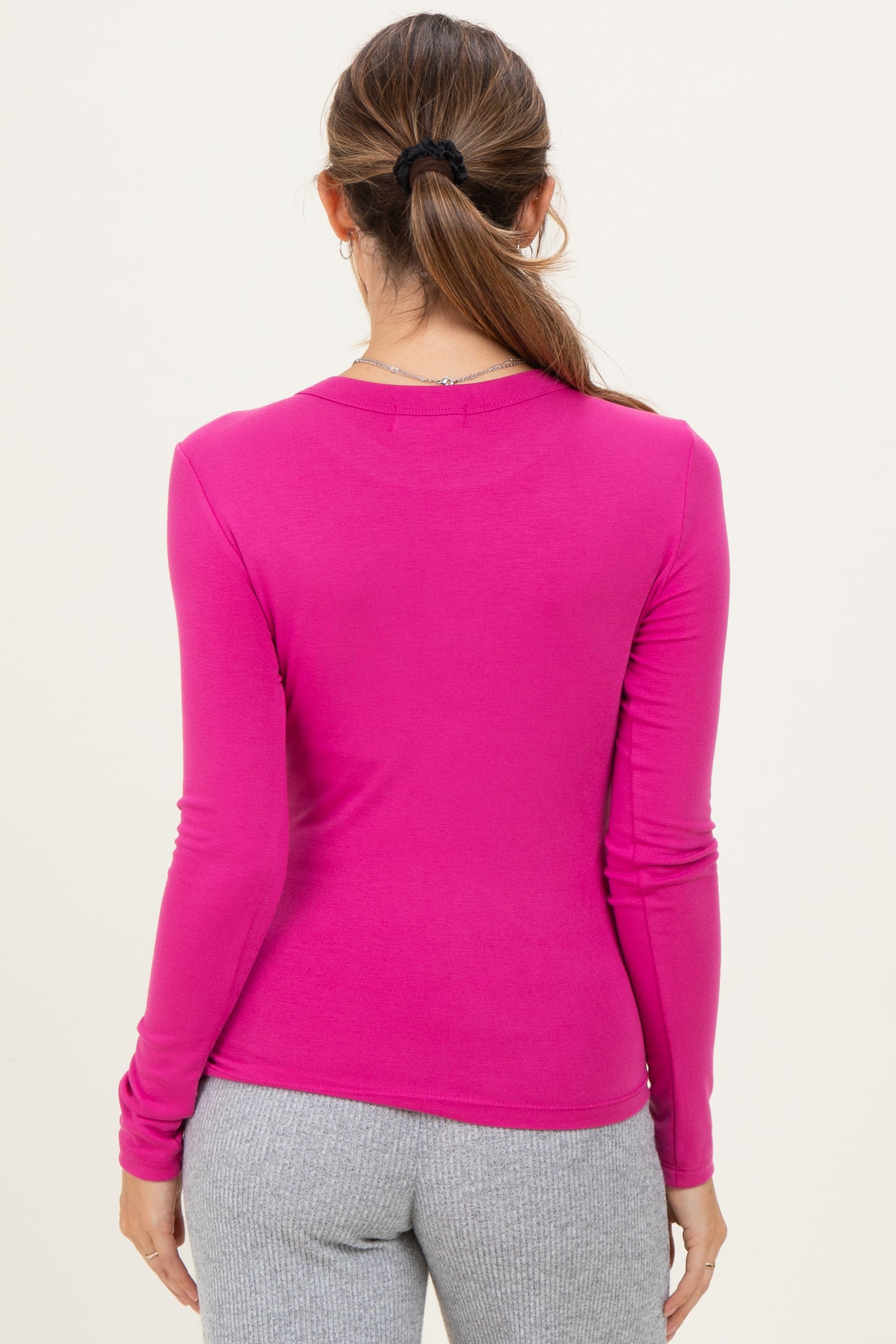 woman wearing a fitted pink long sleeve maternity top, back view, paired with gray leggings