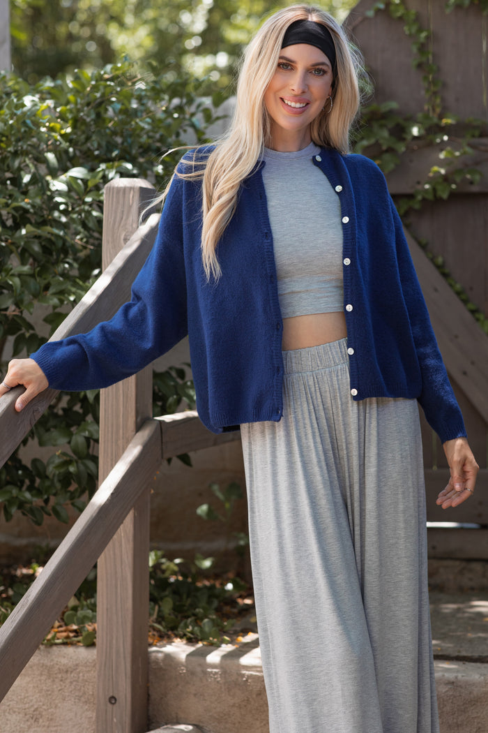 woman wearing a navy blue cardigan over a gray crop top, paired with gray wide-leg pants, smiling outdoors