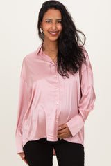 woman wearing a light pink satin maternity shirt, showing her baby bump with a smiling expression