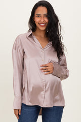 woman wearing a light pink satin maternity button-up shirt and holding her baby bump