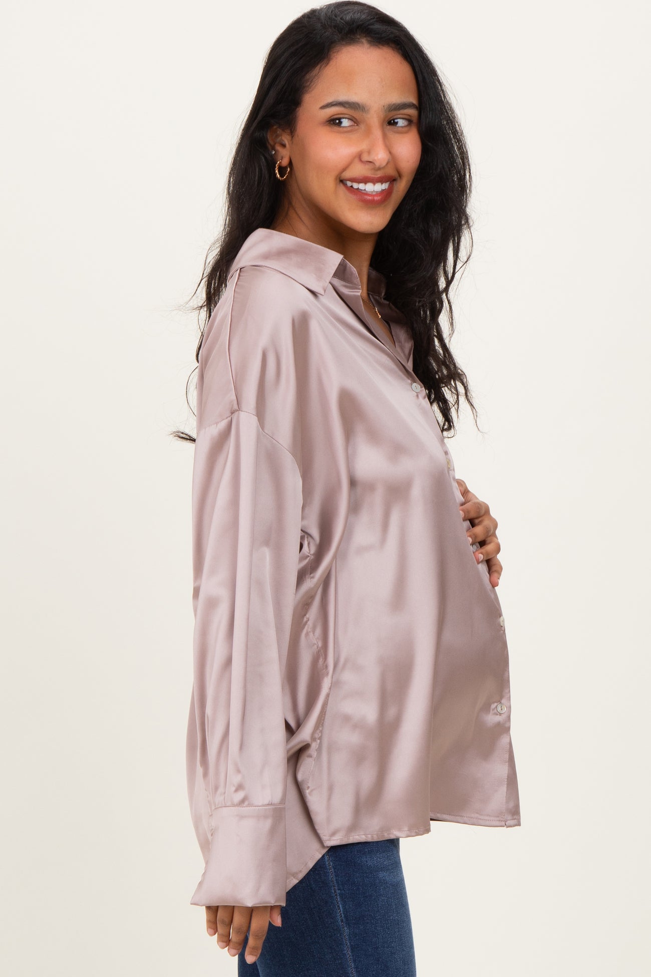 woman wearing a blush satin maternity button-up shirt and showing her baby bump