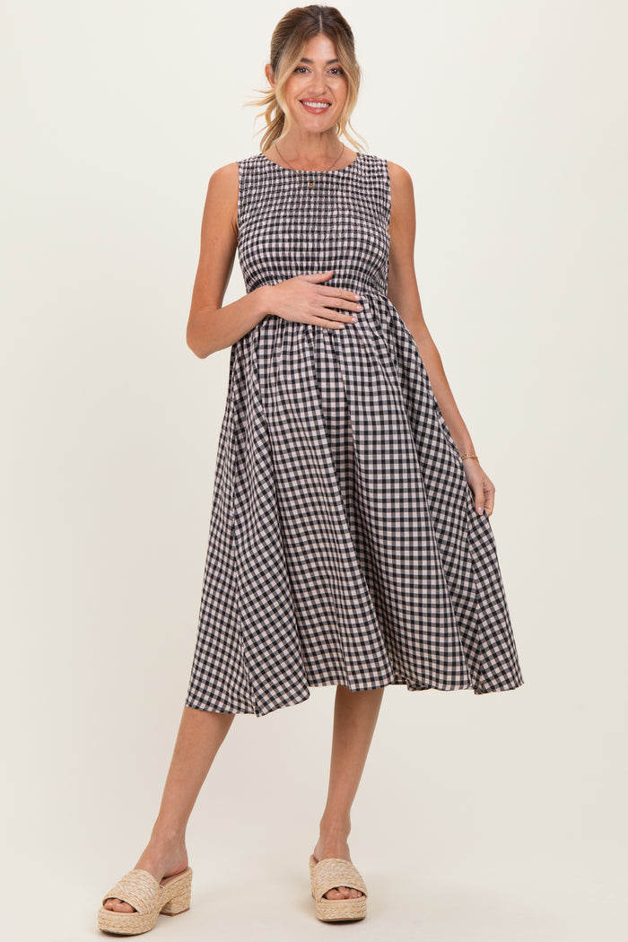 woman wearing a black and white gingham sleeveless maternity dress and holding her baby bump