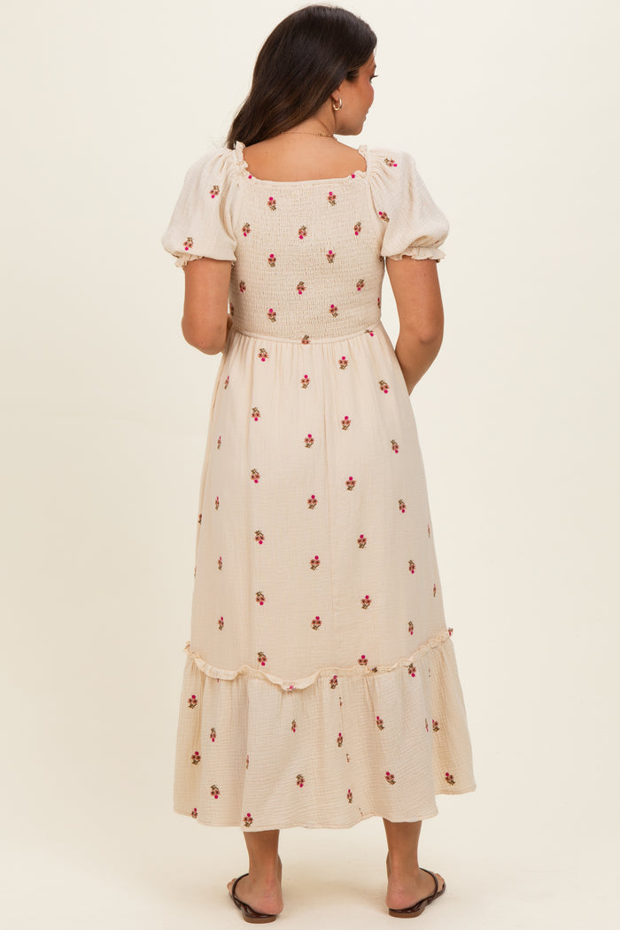 woman wearing a beige maternity dress with floral embroidery and a ruffled hem, seen from the back