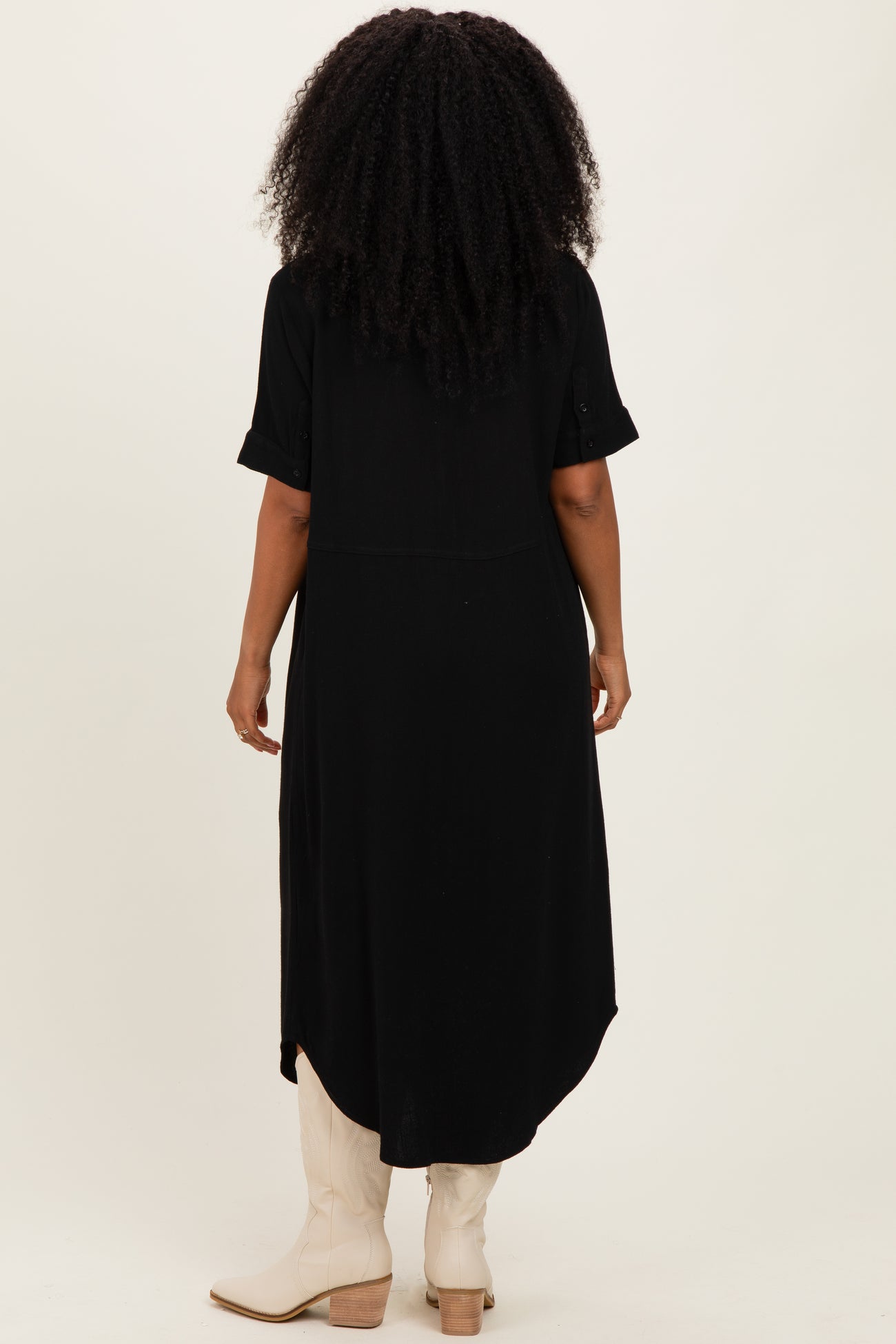 woman wearing a black short sleeve midi dress, viewed from the back, with a curved hem and rolled sleeves