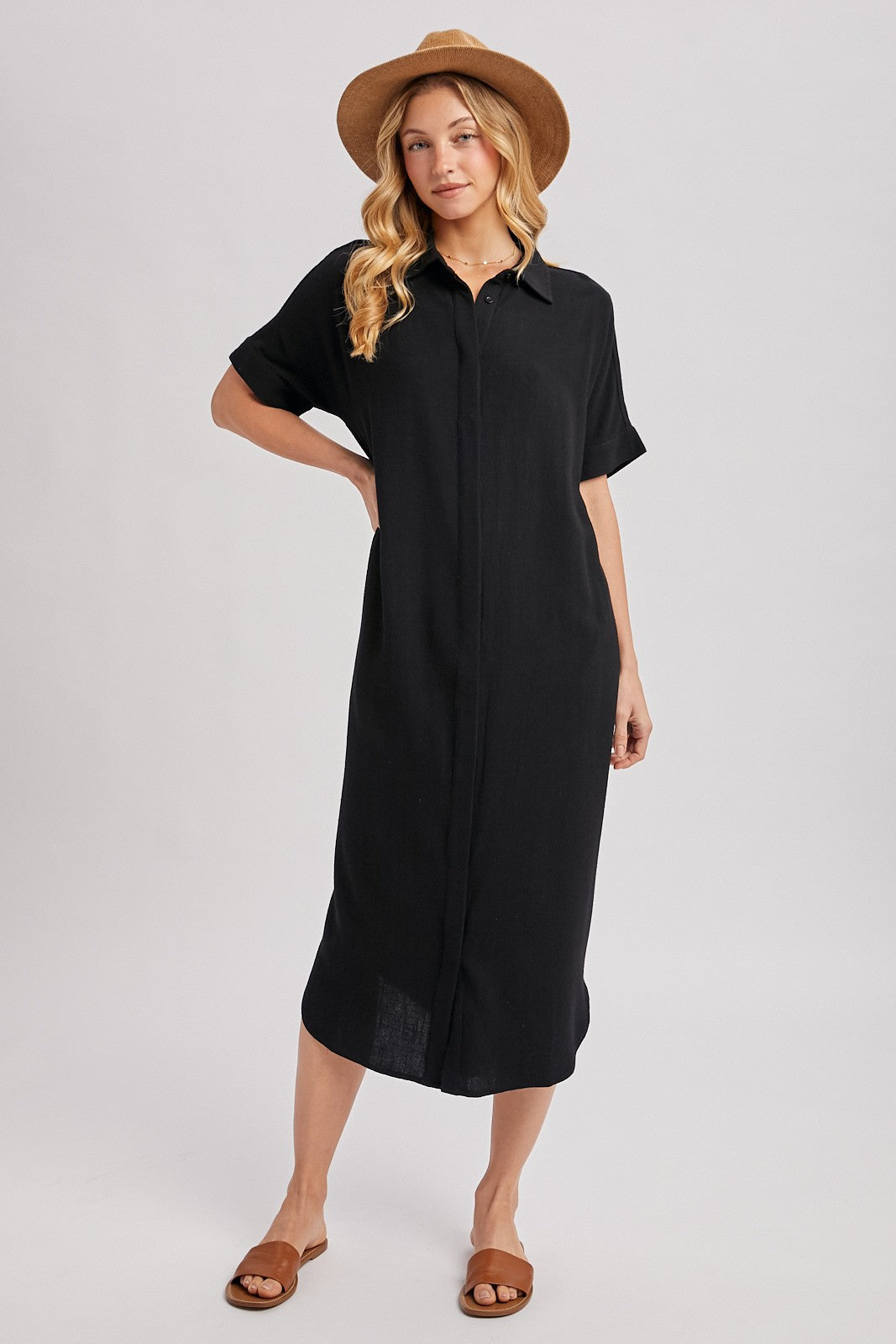 woman wearing a black short sleeve button-up dress and a brown hat, standing with a relaxed pose