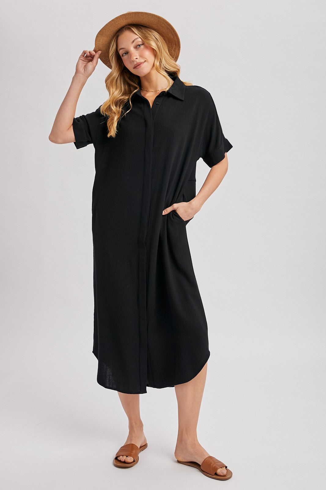 woman wearing a relaxed fit black shirt dress with short sleeves and pockets, paired with a tan hat and brown sandals