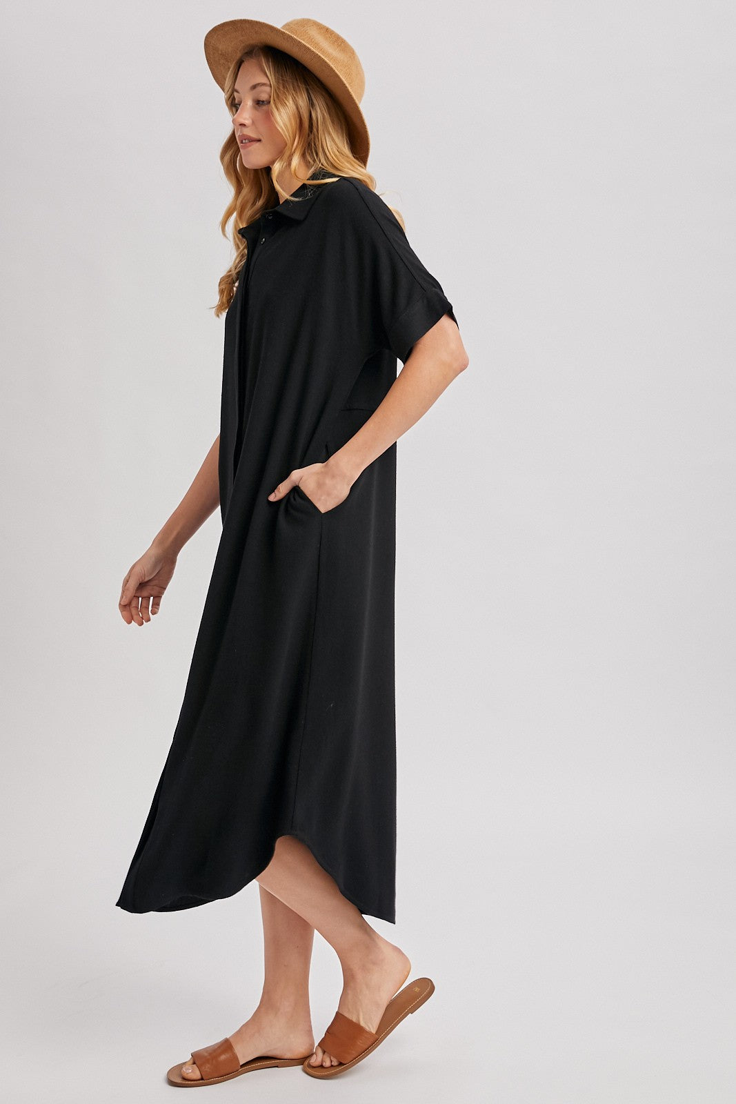 woman wearing a black midi dress with side pockets and a hood, paired with a straw hat and sandals