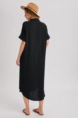 woman wearing a black oversized shirt dress with rolled sleeves and a straw hat, viewed from the back