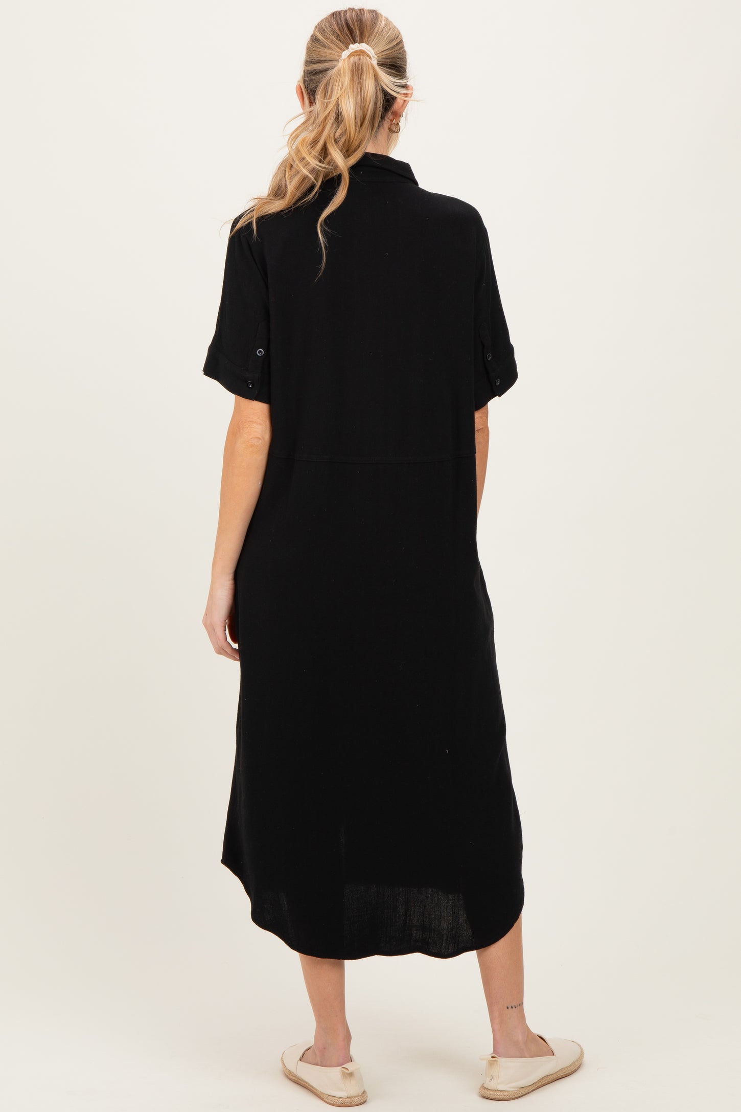 woman wearing a black short sleeve maternity dress, shown from the back, with a relaxed fit and knee-length design