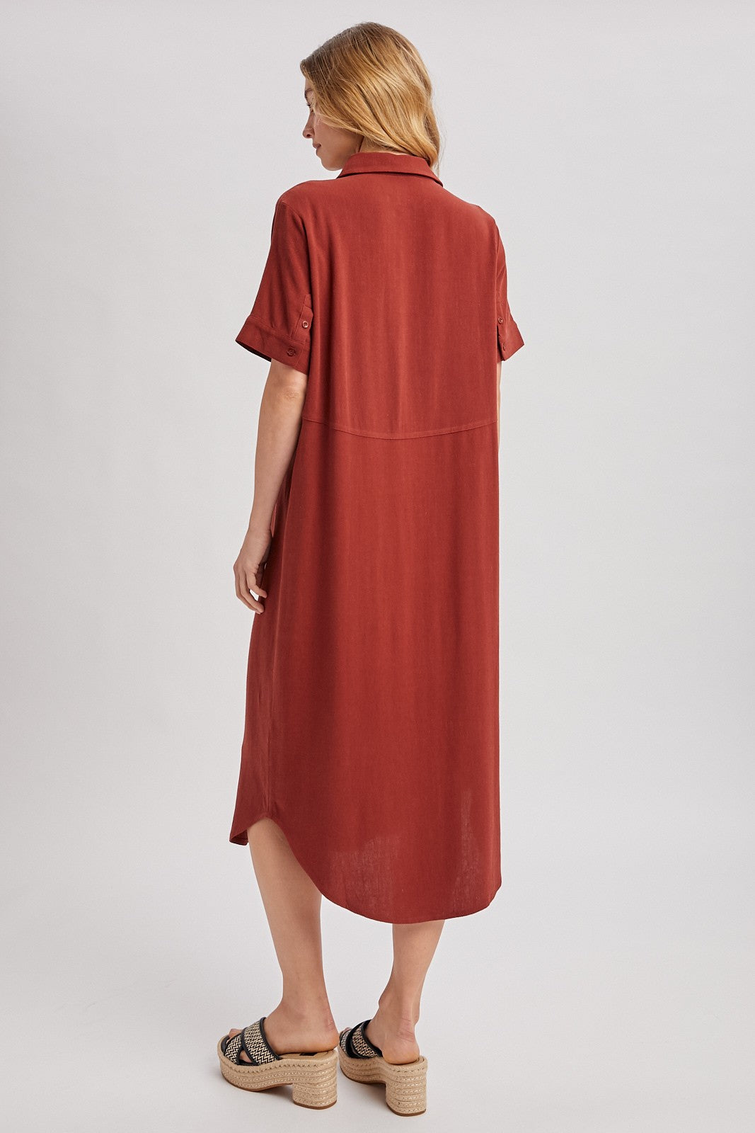 woman wearing a rust-colored short sleeve midi shirt dress and tan platform sandals, view from the back