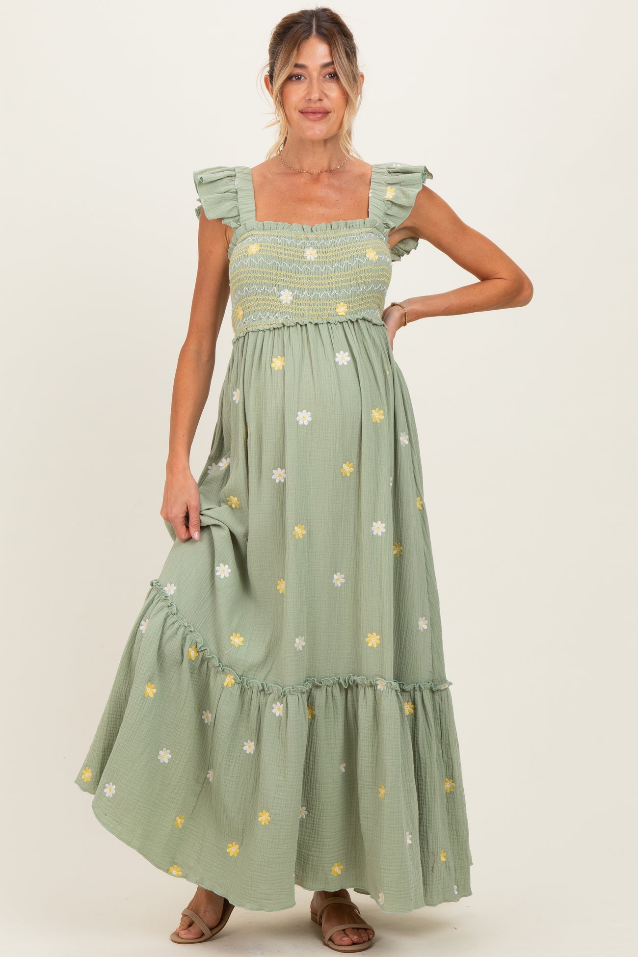 woman wearing a verde green floral embroidered maternity maxi dress with ruffle straps and a fitted bodice