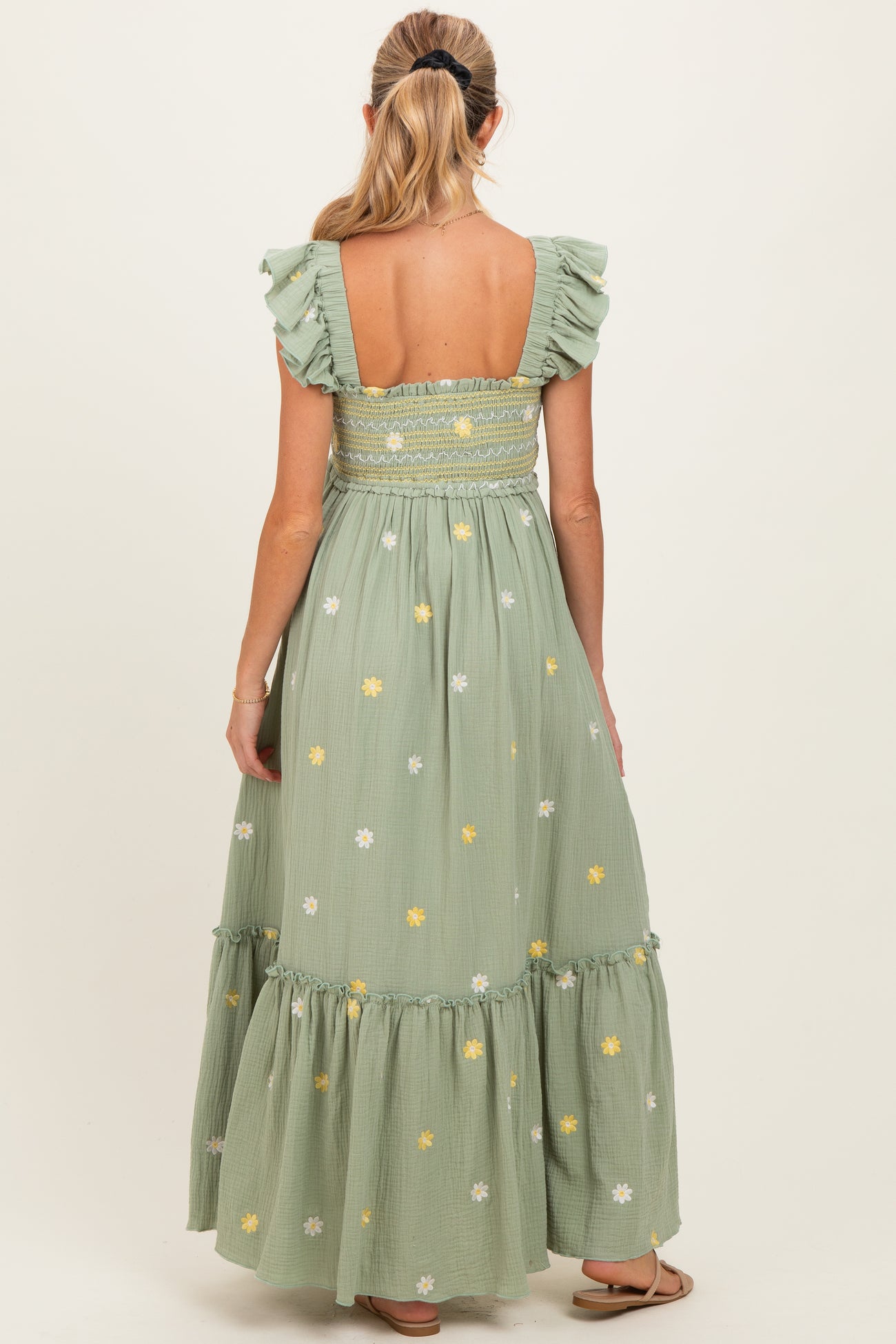 woman wearing a green floral maternity maxi dress with ruffled sleeves and an open back, showing her baby bump