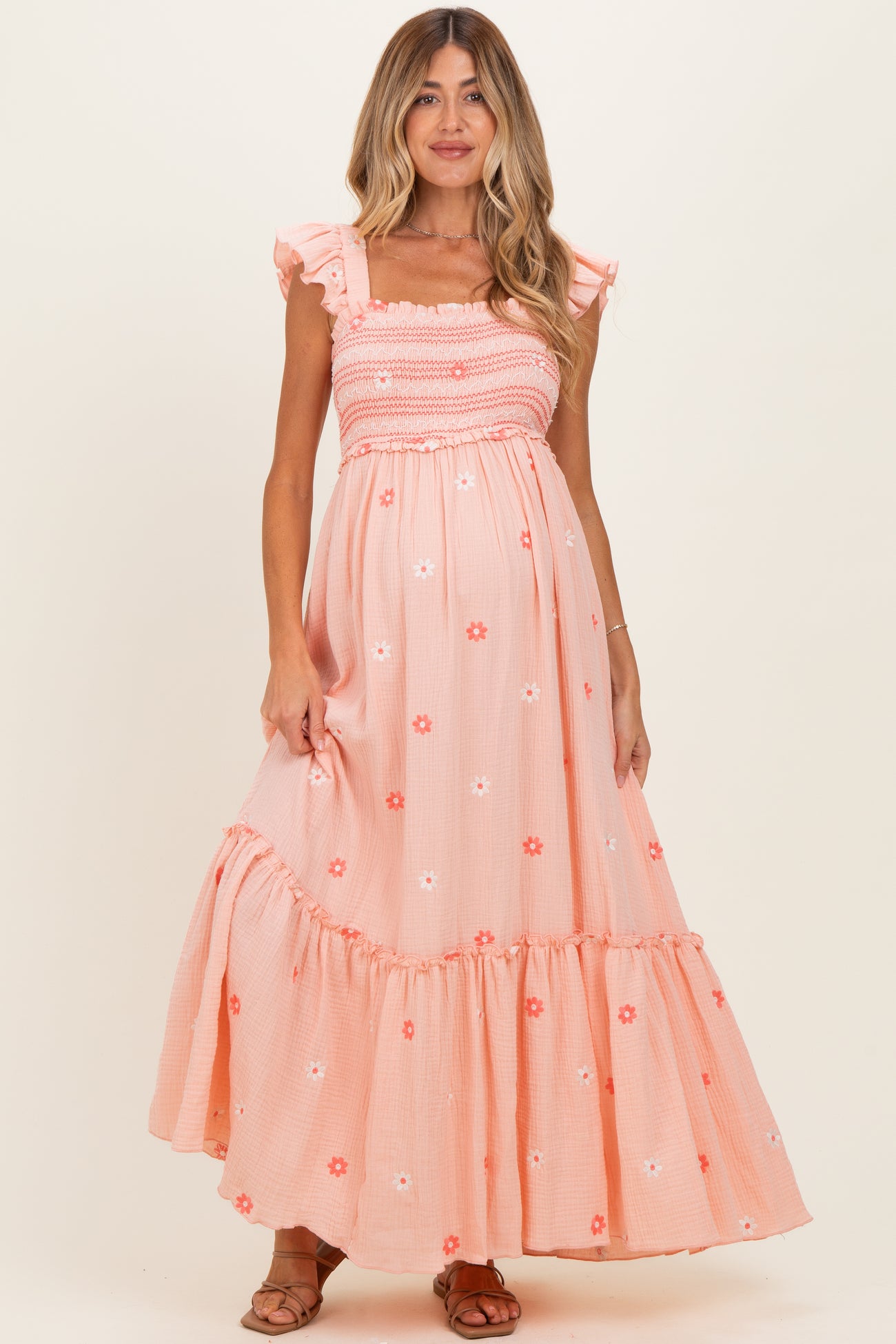 woman wearing a coral floral print maternity maxi dress with ruffled sleeves and a smocked bodice, showcasing her baby bump