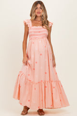 woman wearing a coral floral print maternity maxi dress with ruffled sleeves and a smocked bodice, showcasing her baby bump