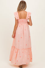 woman wearing a pink floral embroidered maternity maxi dress with ruffle sleeves and a smocked bodice