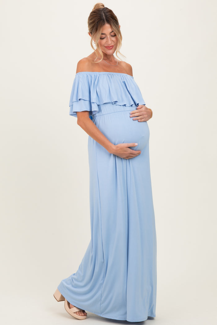 woman wearing a light blue off-the-shoulder maternity gown with ruffle details and holding her baby bump