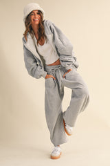 woman wearing a gray oversized jacket and matching sweatpants with a white tank top and a cozy hat